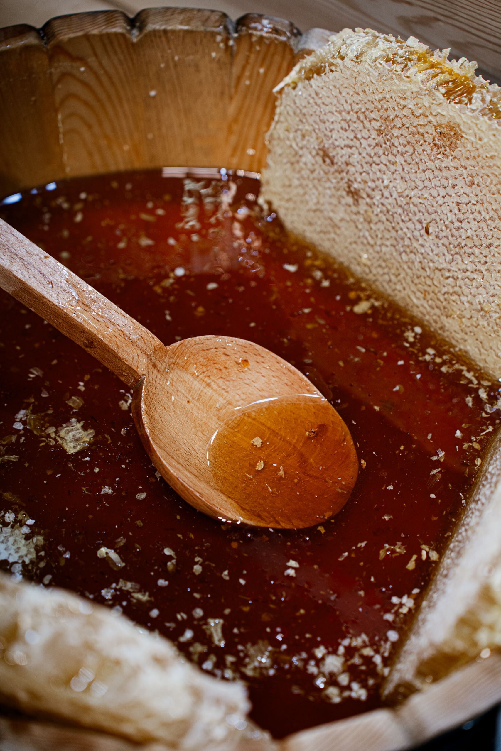 Detailed view of fresh honey in a honeycomb with a wooden spoon highlighting natural sweetness.